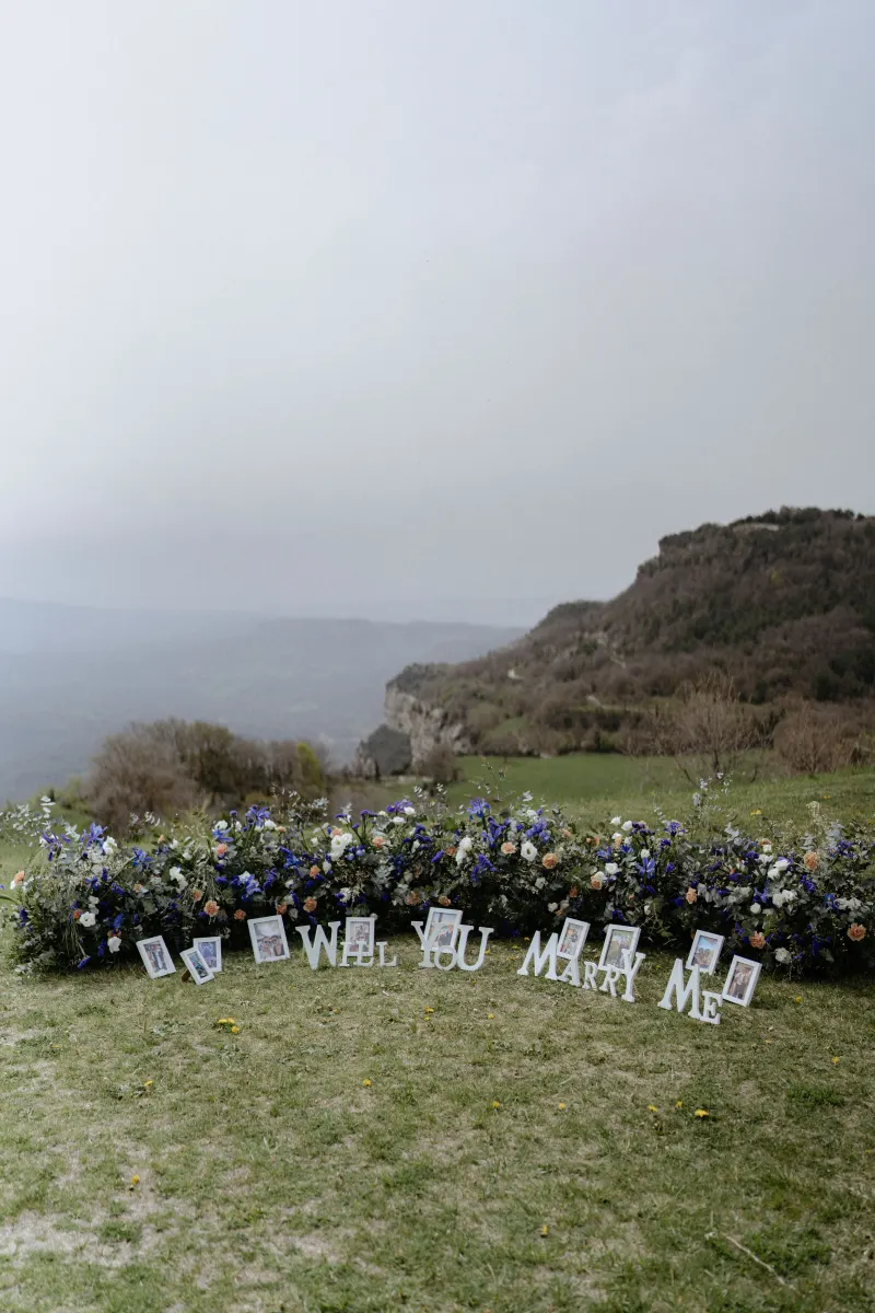 Romantic proposal setup with “Will You Marry Me” letters and flowers on a scenic hillside, perfect for a surprise photoshoot.