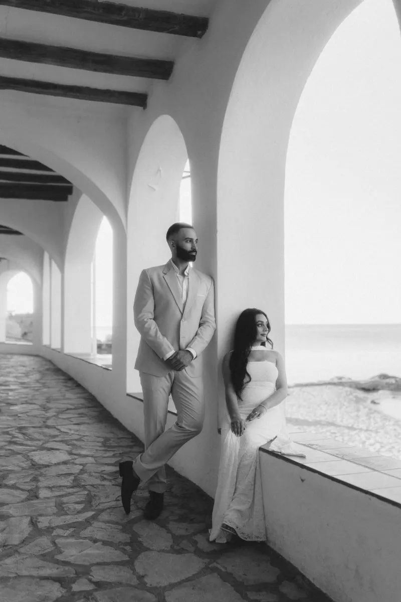 Romantic surprise proposal photoshoot by the beach, capturing a couple’s quiet moment under elegant arches.