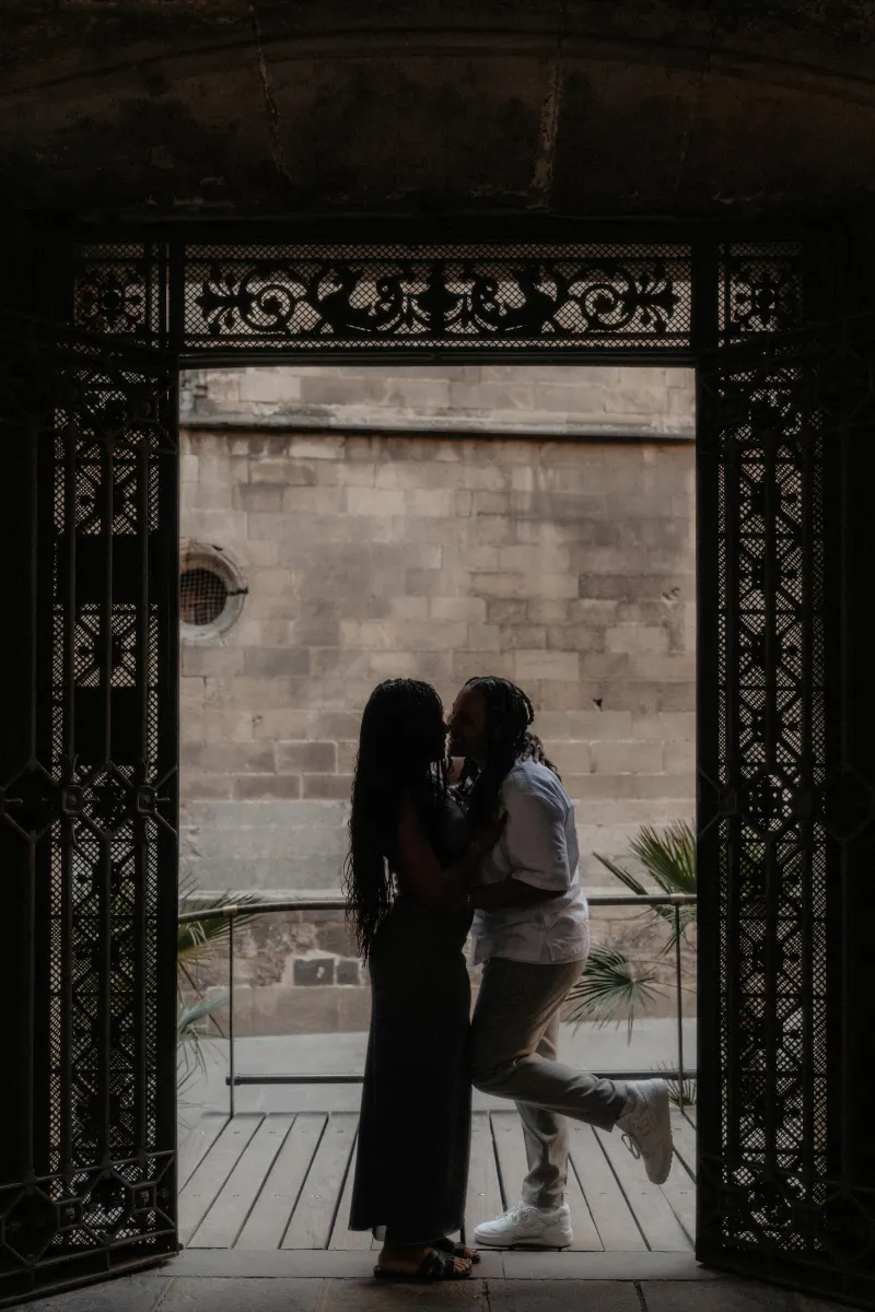Silhouetted couple shares a joyful embrace under ornate gates during a surprise proposal photoshoot in Barcelona.