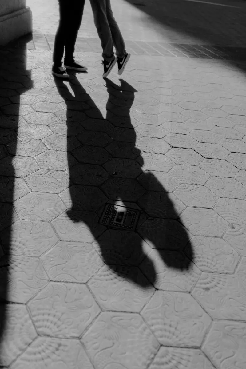 Silhouetted couple shares a quiet moment, their shadows touching on sunlit pavement during an engagement session.