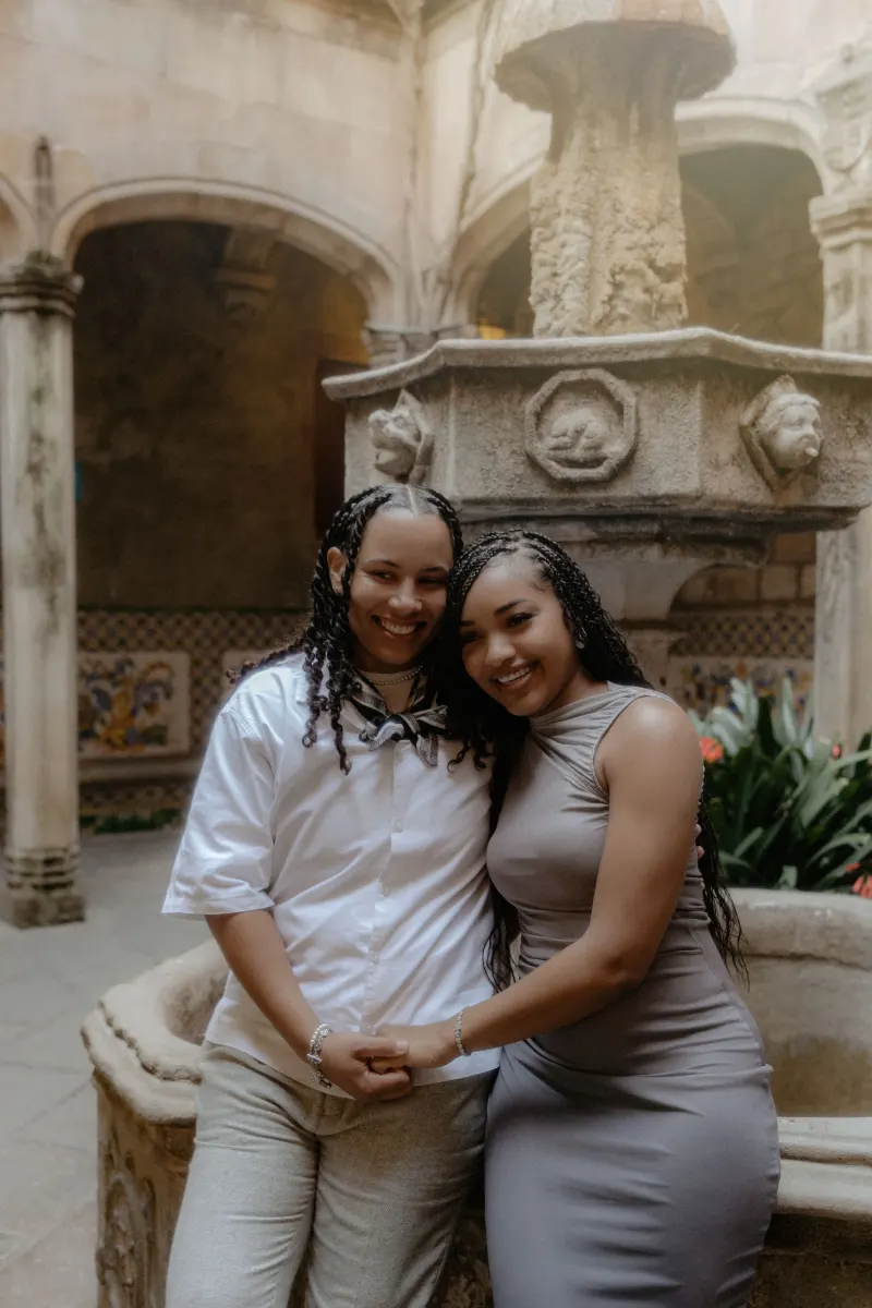 Smiling couple embraces by a historic stone fountain in Barcelona during a surprise proposal photoshoot.