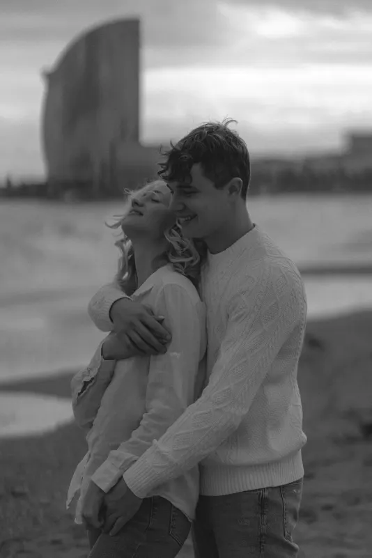 Smiling couple embraces on a beach at sunset, captured during a couples & engagements photoshoot in Barcelona.