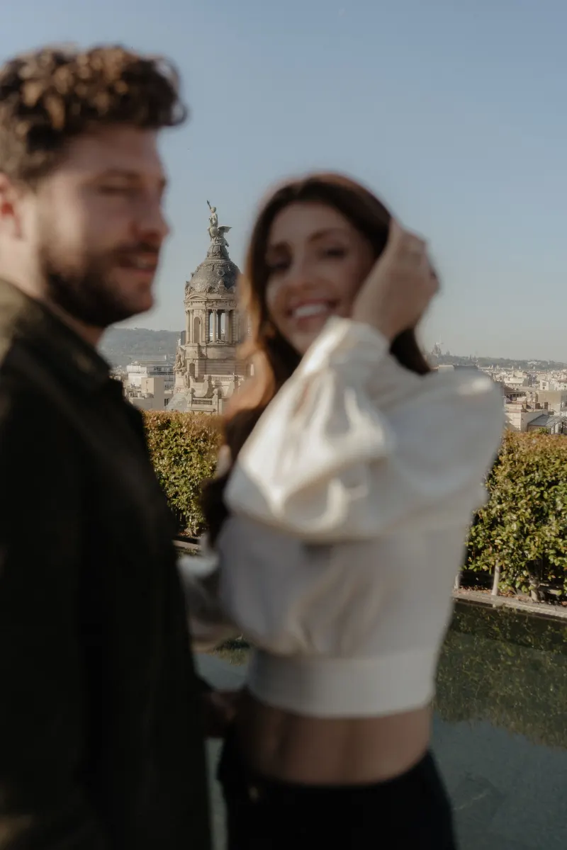 Smiling couple enjoys a relaxed moment on a rooftop during a couples & engagements photoshoot with city views.