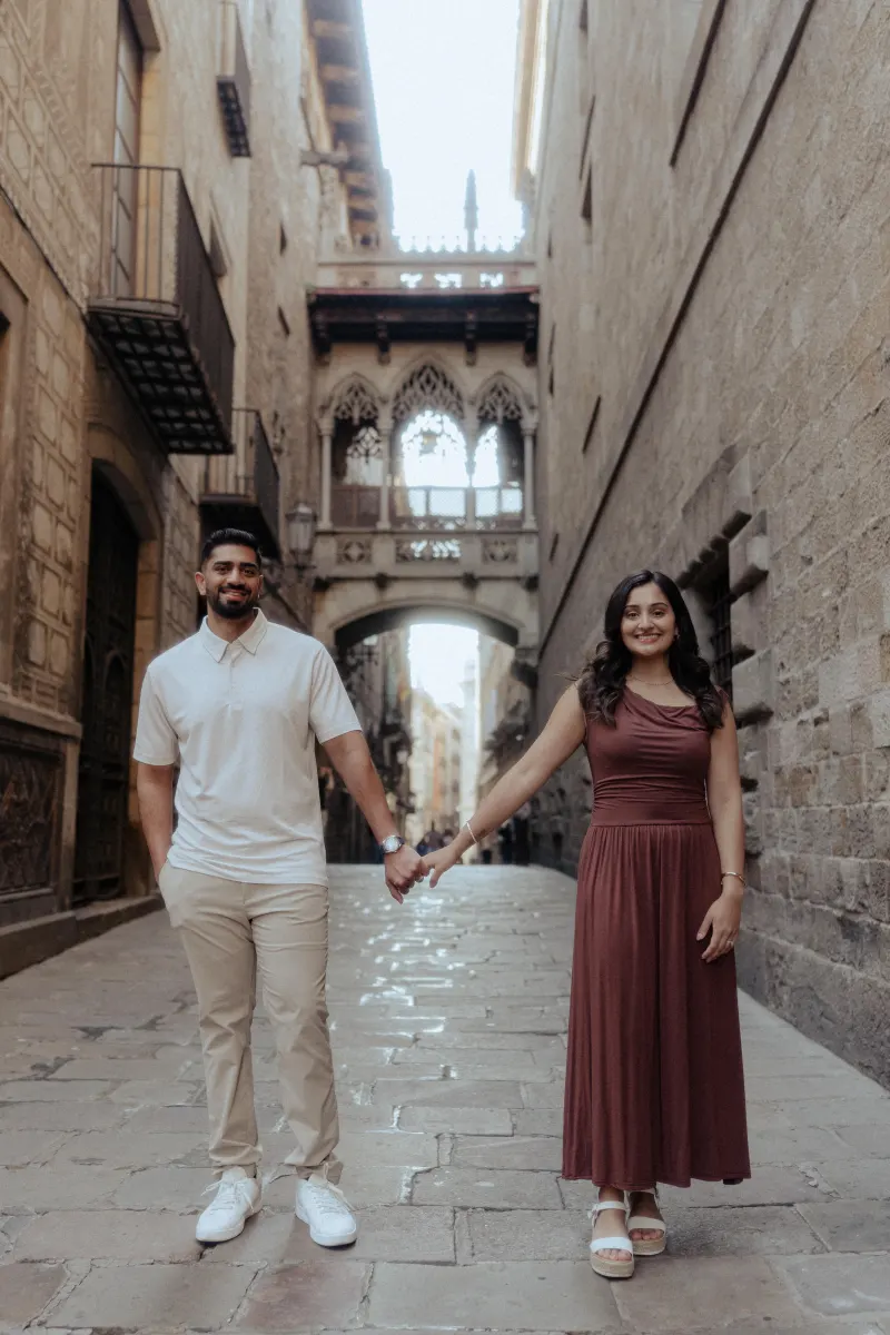 Smiling couple holding hands in a historic European alleyway during a couples & engagements photoshoot.