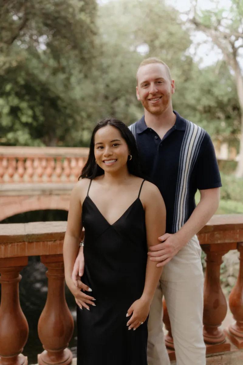 Smiling couple poses together on a garden bridge after their surprise proposal, captured during a professional photoshoot.