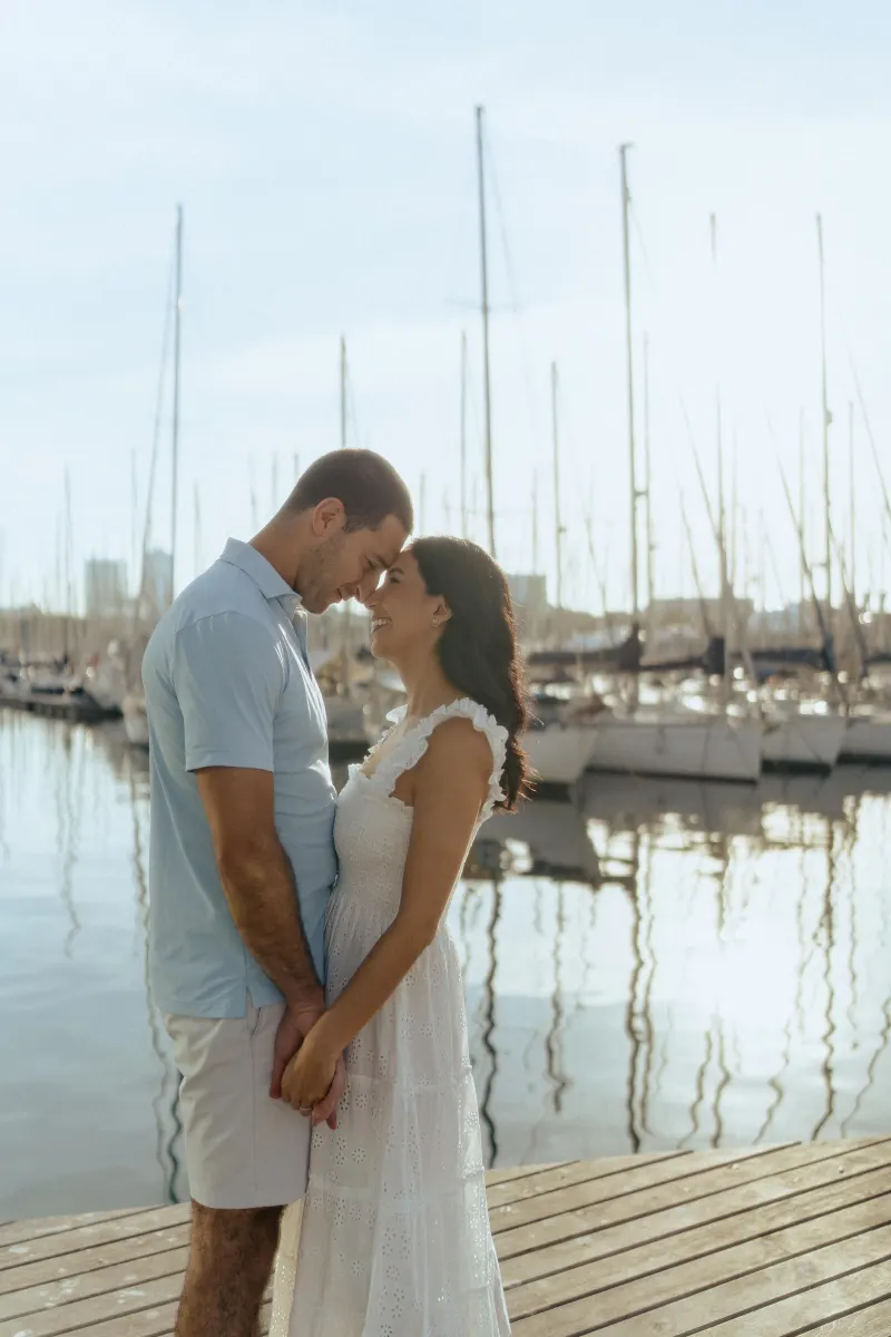 Smiling couple shares a tender moment on a marina dock, captured during a couples & engagements photoshoot.