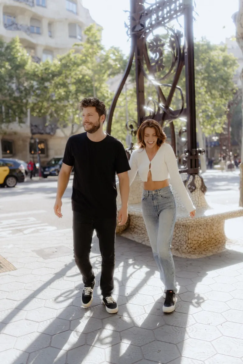 Smiling couple strolls hand in hand through sunlit city streets during a couples & engagements photoshoot.