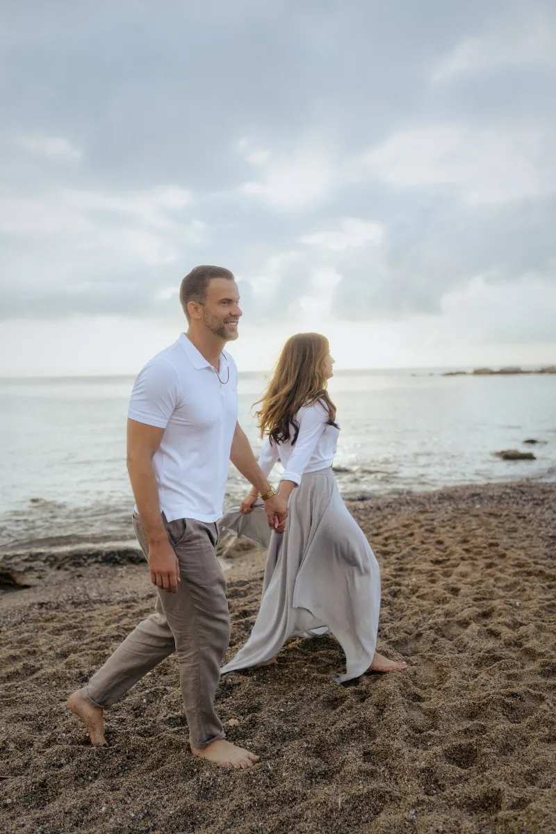 Smiling couple walking hand in hand along the shoreline during a relaxed couples & engagements photoshoot.