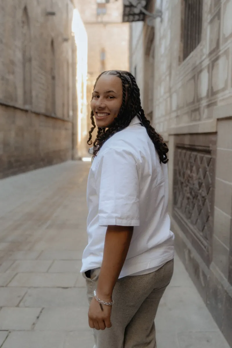 Smiling person glances back while strolling through a sunlit alley in Barcelona during a surprise proposal photoshoot.