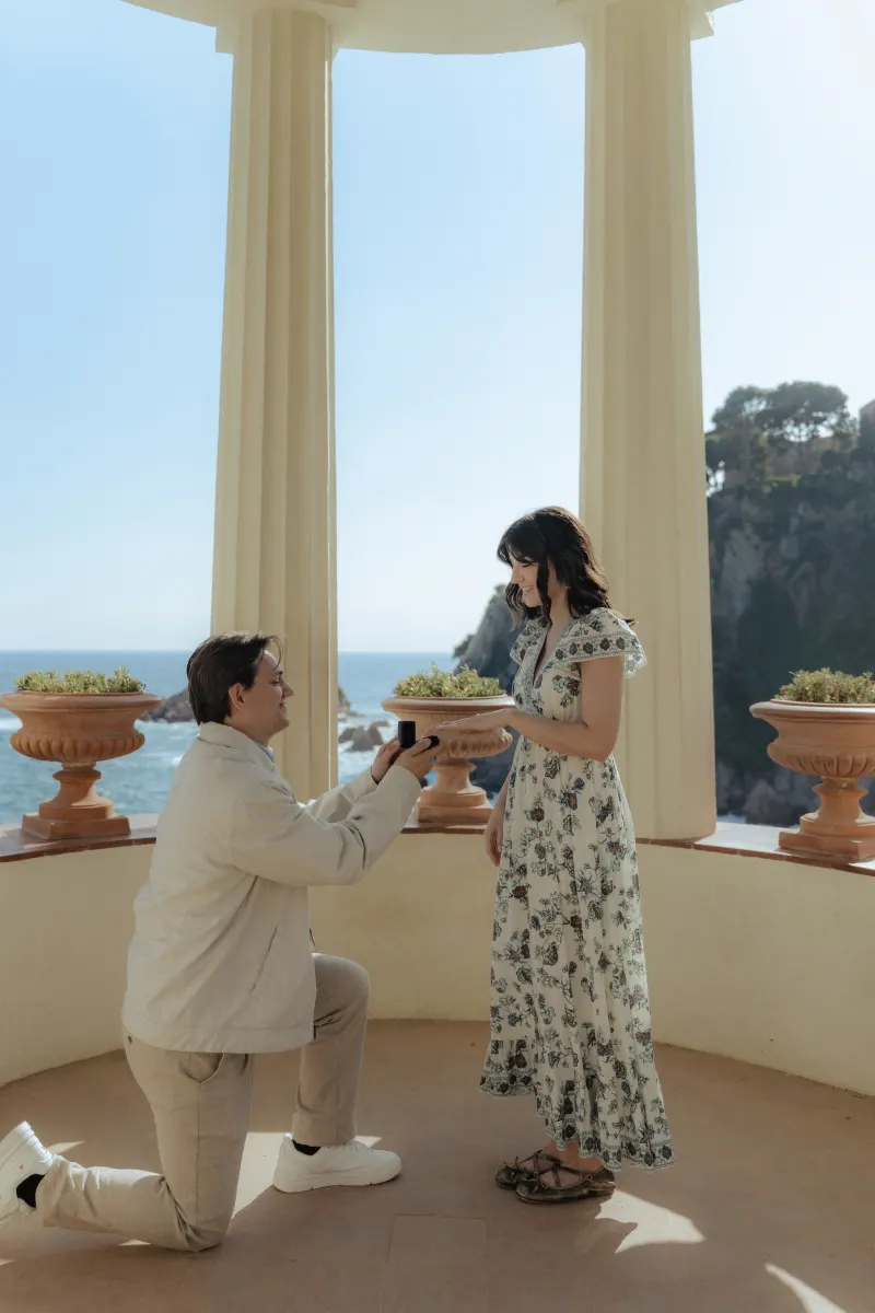 Surprise proposal photography capturing a heartfelt moment as he proposes under a seaside pavilion.