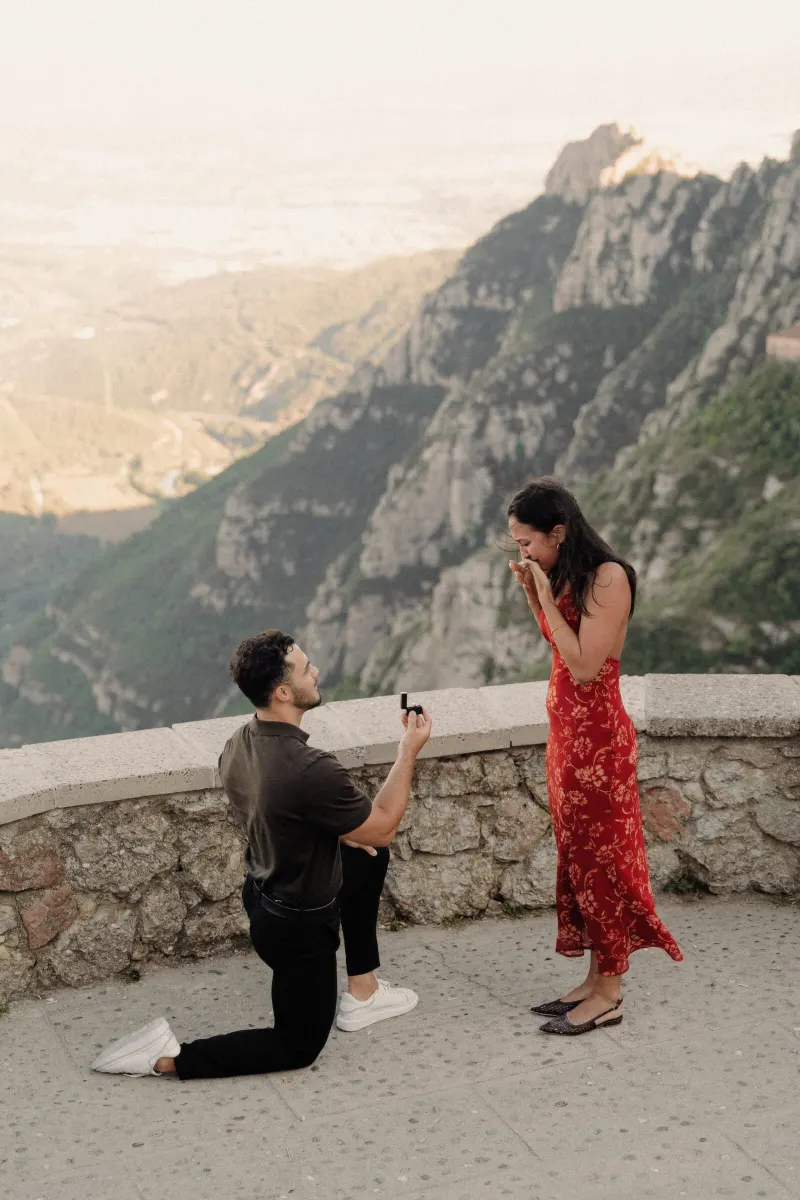 Sydney covers her face in disbelief while Dan proposes at a scenic Montserrat viewpoint.