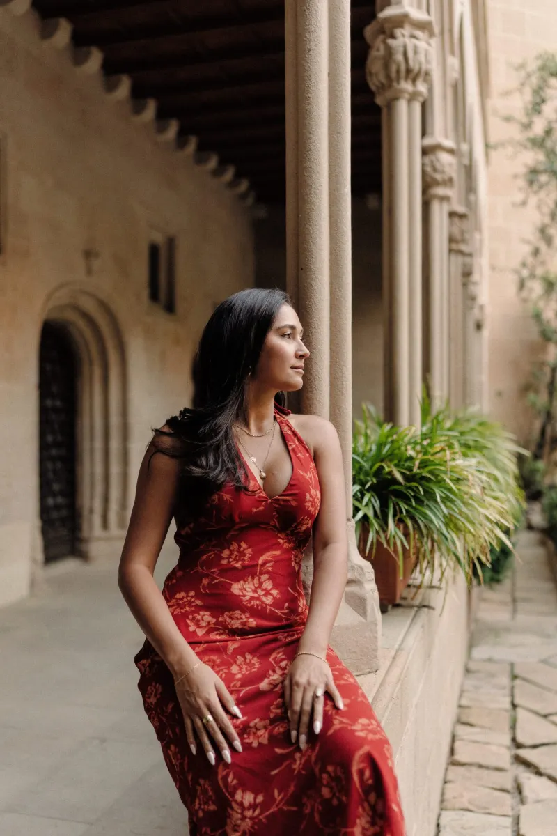 Sydney in her red lace dress sits beside the stone columns of the Montserrat monastery.