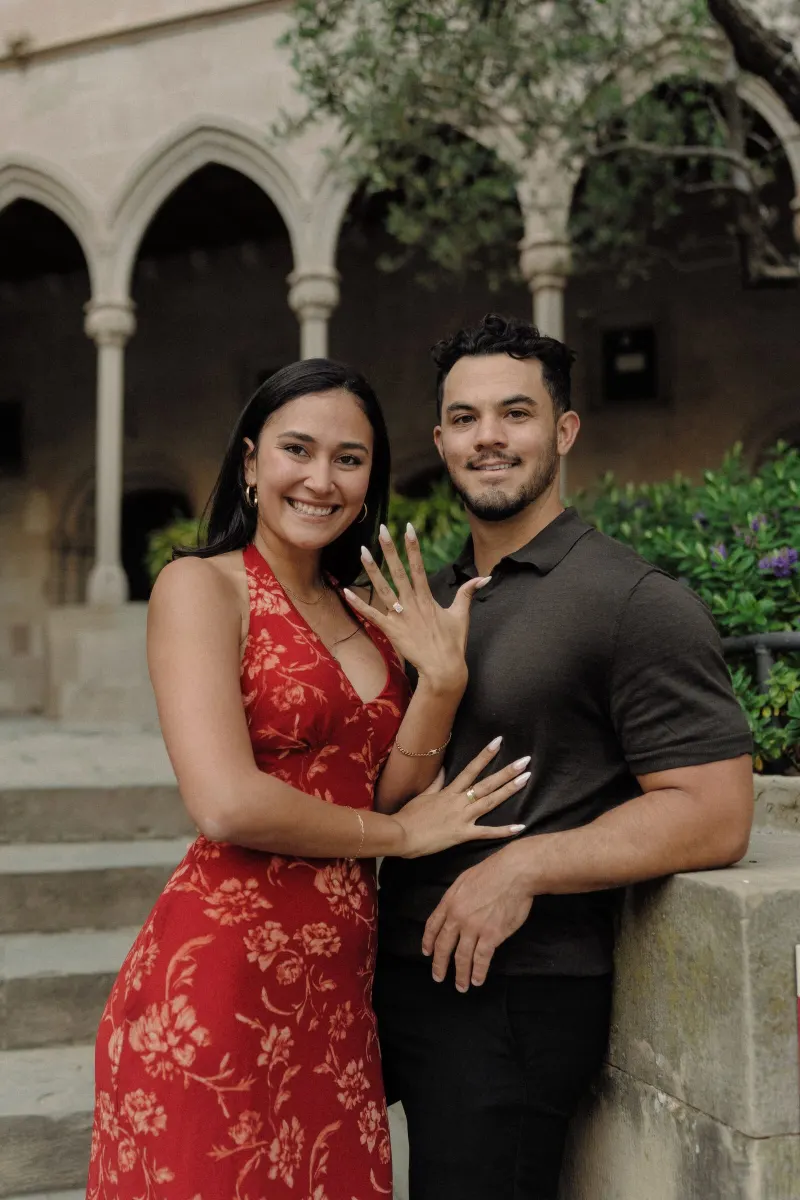 Sydney shows her engagement ring as she and Dan smile for a portrait in the monastery courtyard.