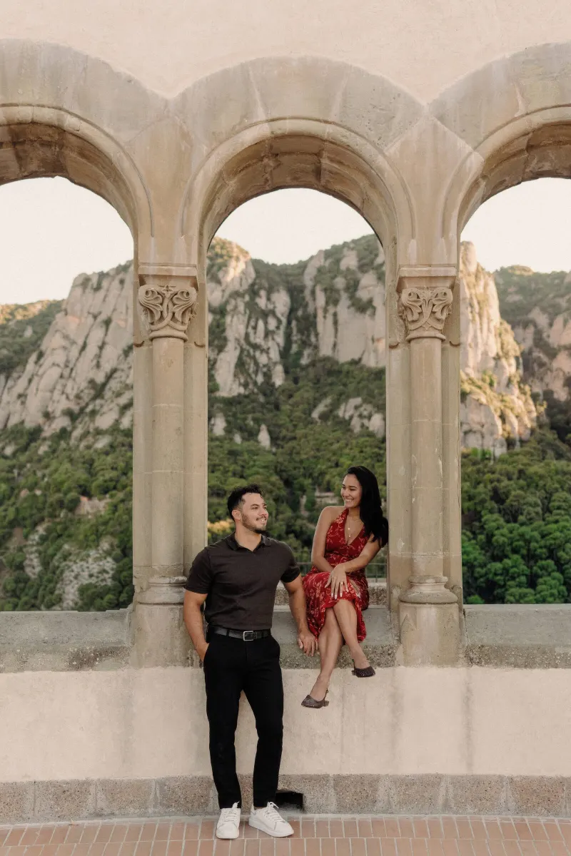 Sydney sits beneath a stone arch while Dan stands beside her during their Montserrat engagement session.