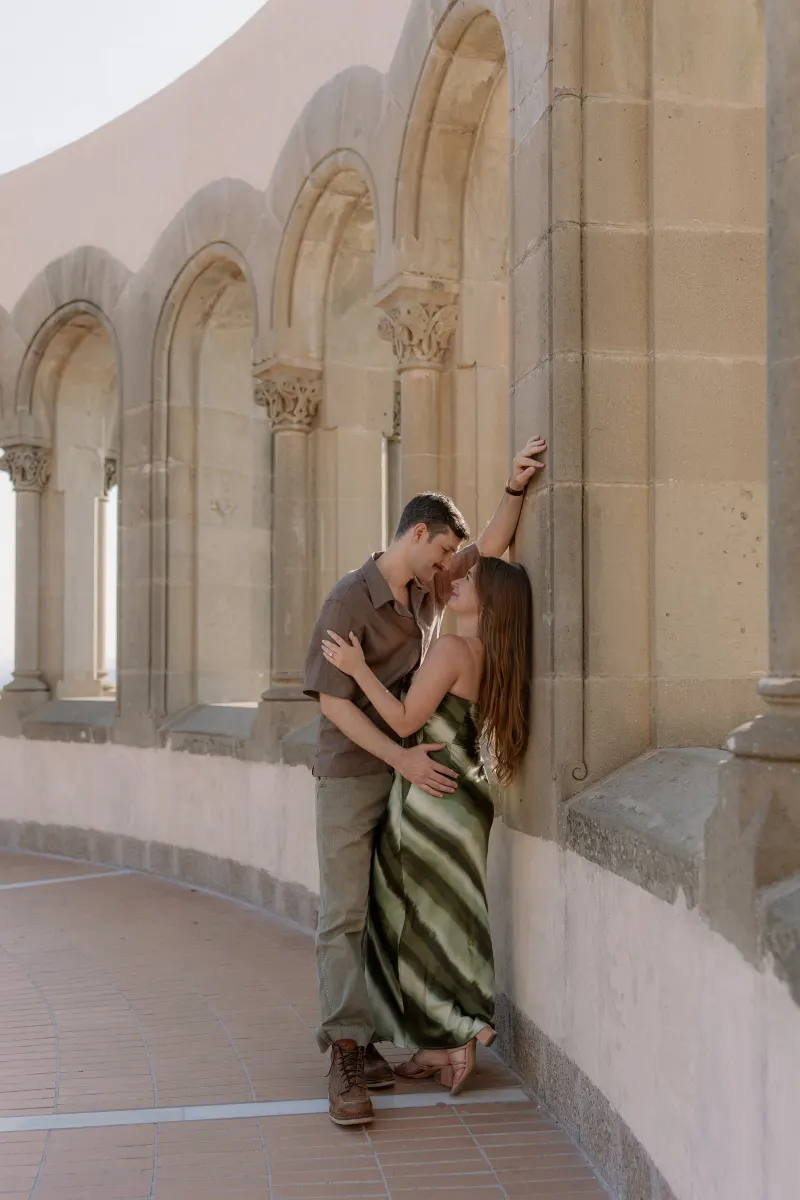 Tim and Megan kiss beside a column in the curved gallery.