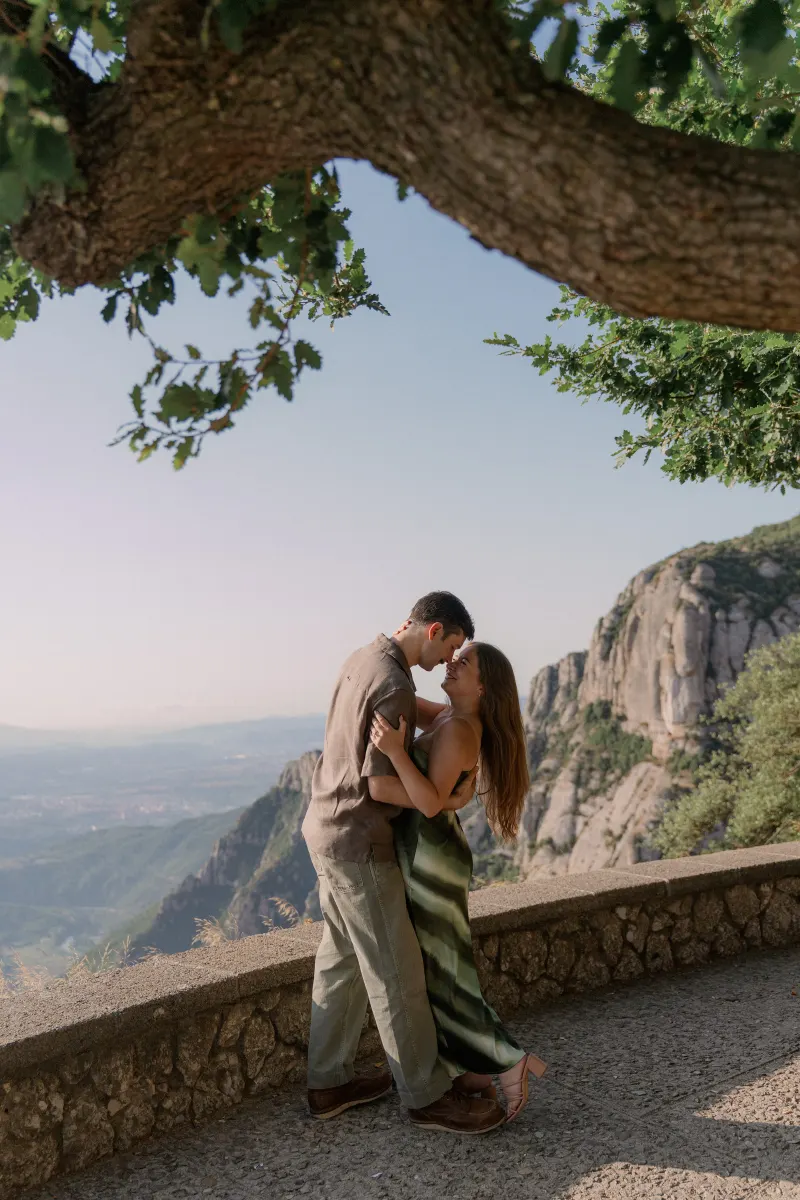 Tim and Megan kiss under the branches at the mountain viewpoint.