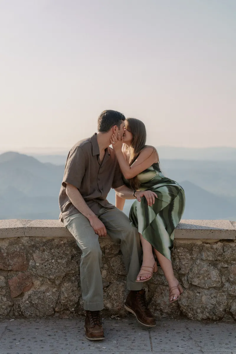 Tim and Megan kiss while sitting together on the stone parapet.