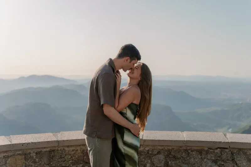 Tim and Megan share a kiss with layered hills in the background.