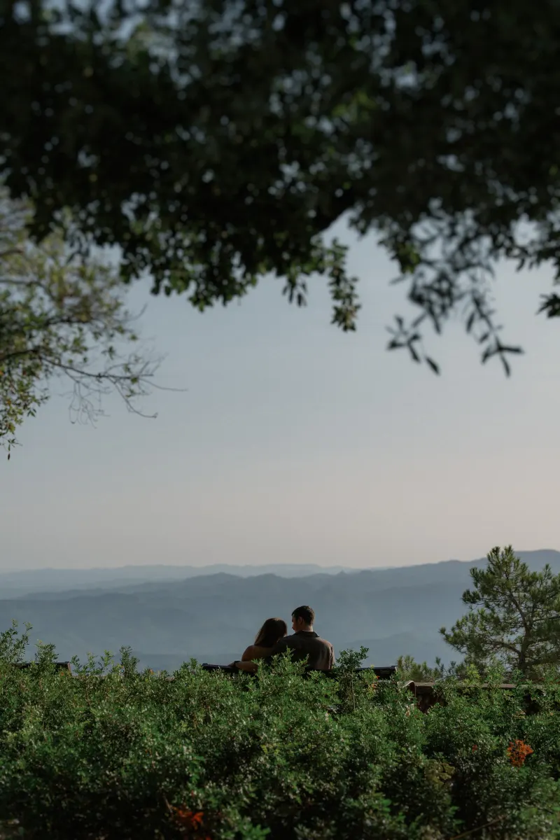 Tim and Megan sit beneath a large tree with the valley in the distance.