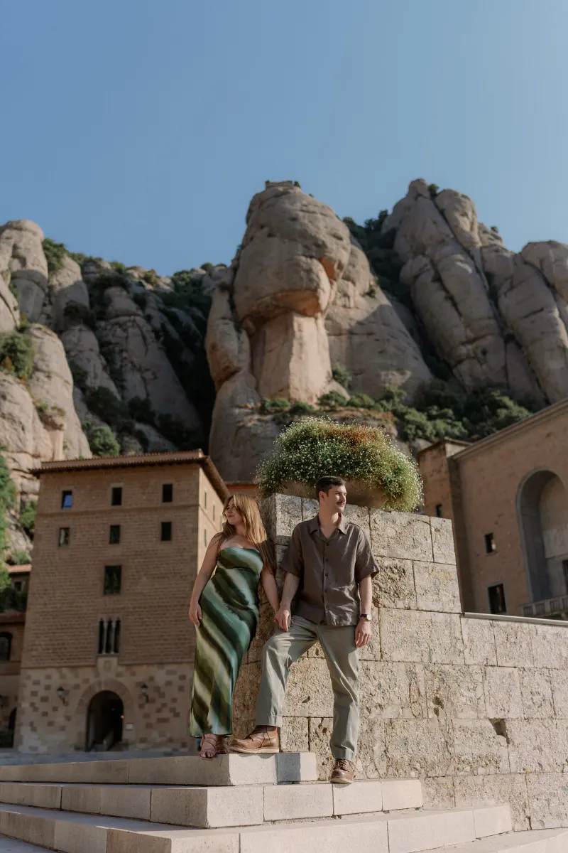 Tim and Megan stand on stone steps beneath Montserrat's rounded peaks.