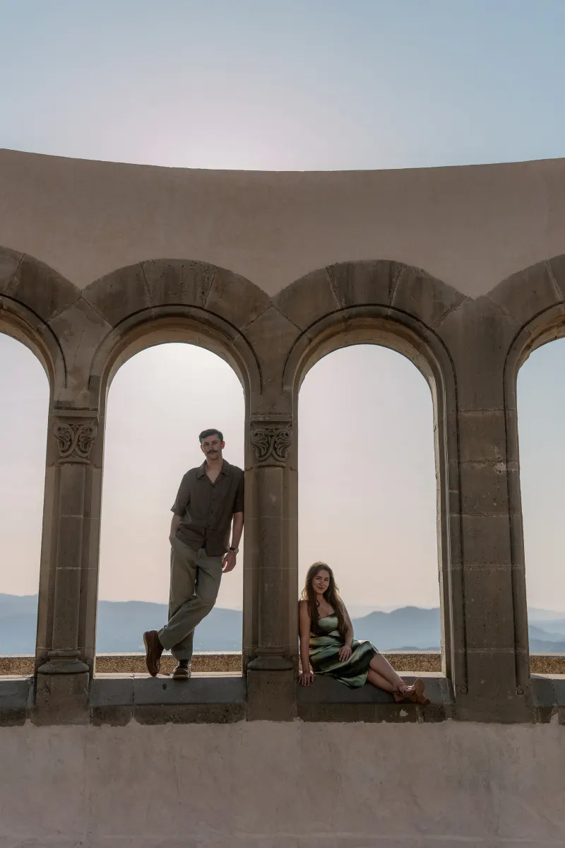 Tim leans against an arch while Megan sits in the neighboring opening.