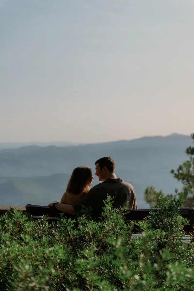 Tim rests his arm around Megan on a bench overlooking the mountains.