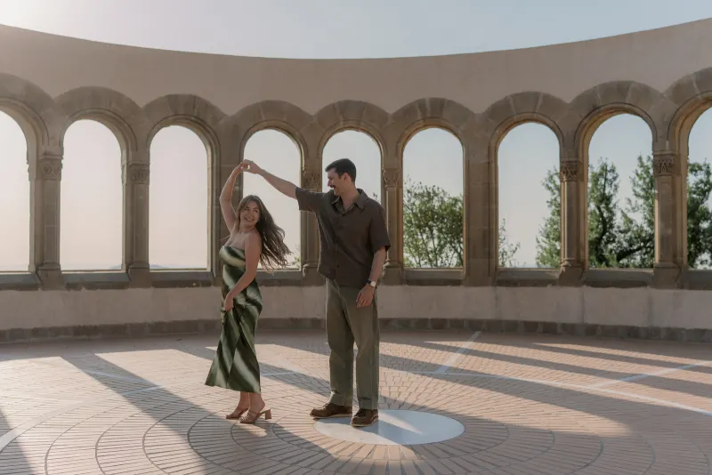 Tim twirls Megan across the sunlit floor between the stone arches.