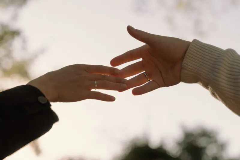 Two hands with matching rings reach for each other at sunset, capturing a tender moment from a couples & engagements shoot.