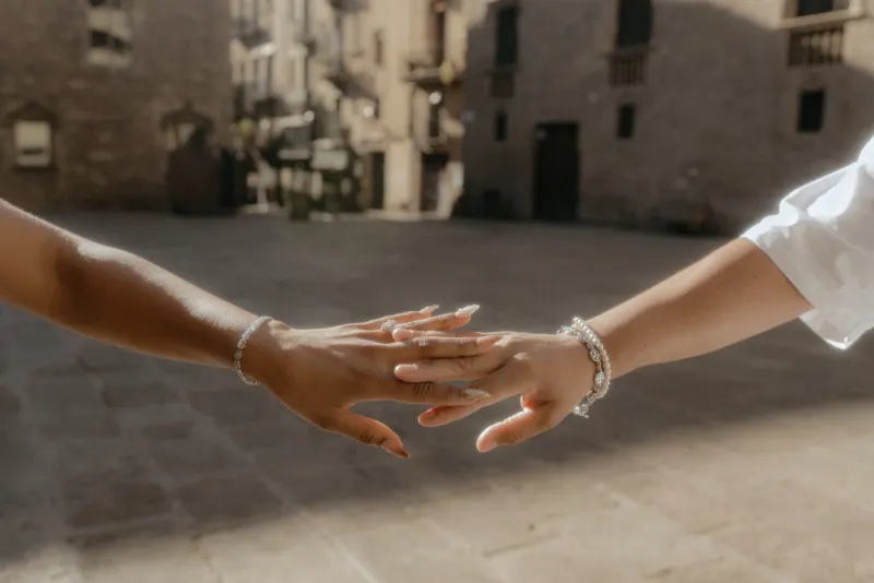 Two partners gently touch hands, showing off an engagement ring during a surprise proposal photoshoot in Barcelona.