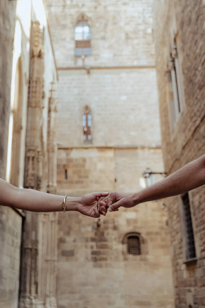 Two people gently reach for each other’s hands during a couples & engagements photoshoot in a historic stone alley.