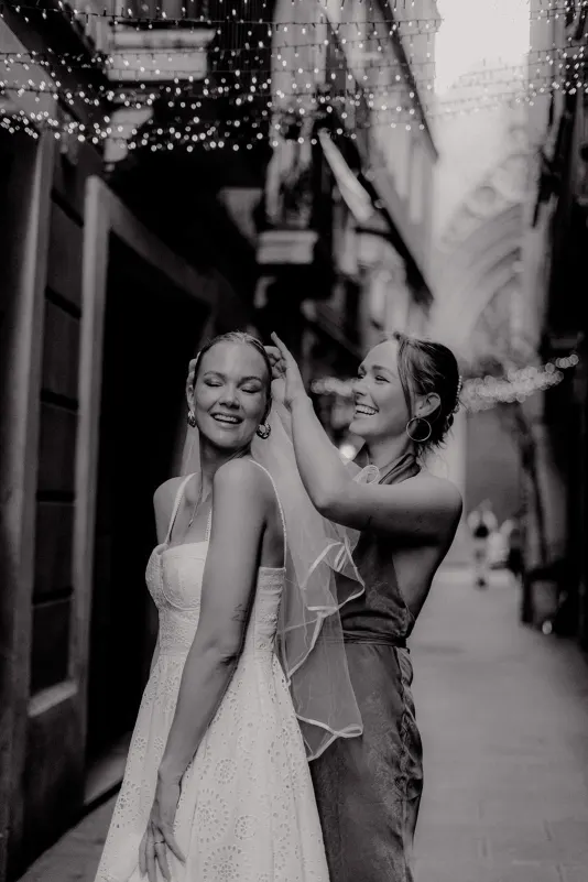 Two women share a joyful moment as one adjusts the other's veil during a Vacation Portraits photoshoot in Barcelona.