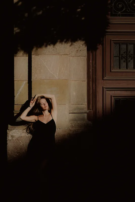 Woman in a black dress basks in golden sunlight against a city wall during a Vacation Portraits photoshoot abroad.