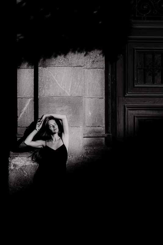 Woman in a black dress basks in sunlight against a stone wall, captured during a Vacation Portraits photoshoot abroad.