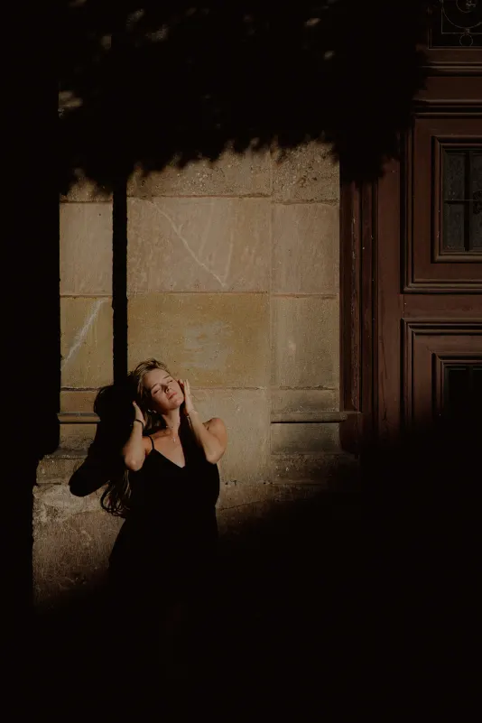 Woman in a black dress enjoys golden sunlight against a city wall during a Vacation Portraits photoshoot.