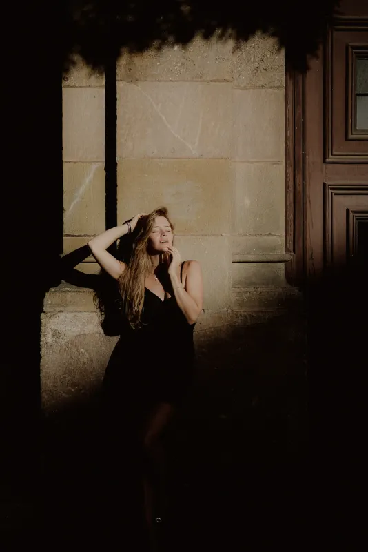 Woman in a black dress enjoys the warm sunlight against a city wall during a Vacation Portraits photoshoot abroad.