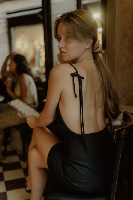 Woman in a black dress glances back over her shoulder at a café table during a Vacation Portraits photoshoot.