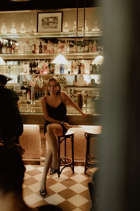 Woman in a black dress laughs at a stylish bar, captured candidly during a Vacation Portraits photoshoot abroad.