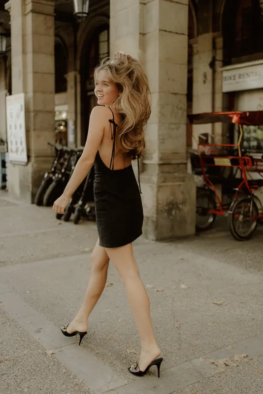 Woman in a black dress laughs while walking past city arches during a Vacation Portraits photoshoot abroad.