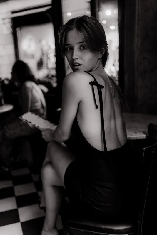 Woman in a black dress looks over her shoulder at a café table, captured during a Vacation Portraits photoshoot in Europe.