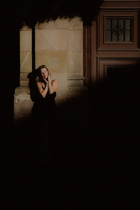 Woman in a black dress poses thoughtfully in dramatic sunlight against a city wall during a Vacation Portraits session.