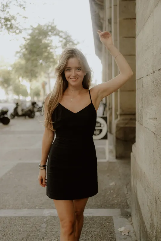 Woman in a black dress smiles and poses by a city wall during a Vacation Portraits photoshoot abroad.