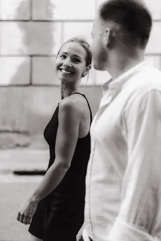 Woman in a black dress smiles brightly at her partner during a candid couples & engagements photoshoot outdoors.