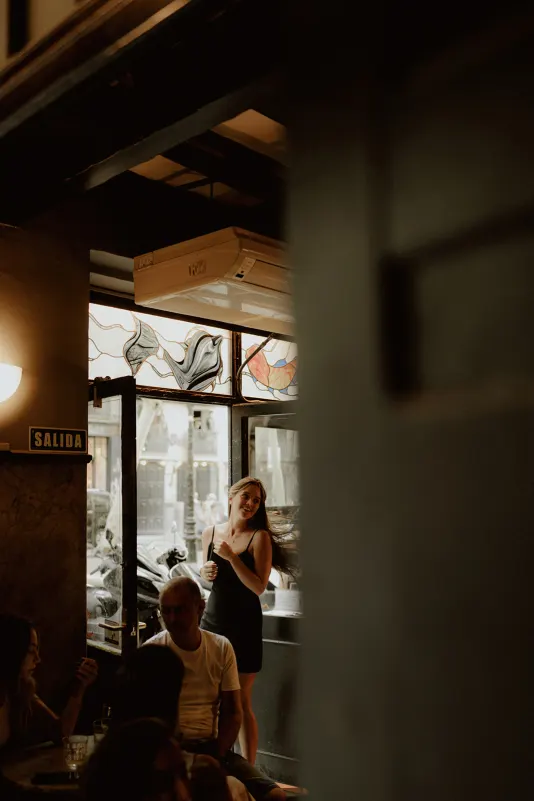 Woman in a black dress smiles by a café doorway, captured candidly during a Vacation Portraits photoshoot abroad.