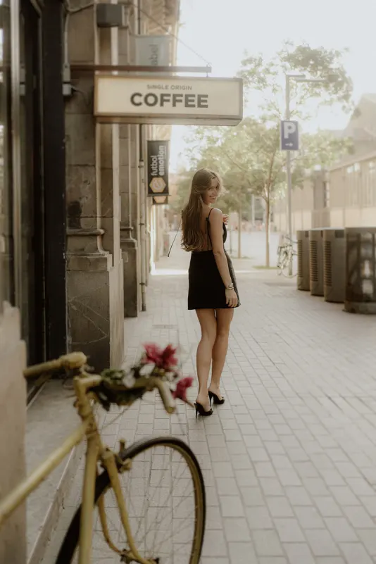 Woman in a black dress smiles over her shoulder on a city street during a Vacation Portraits photoshoot.