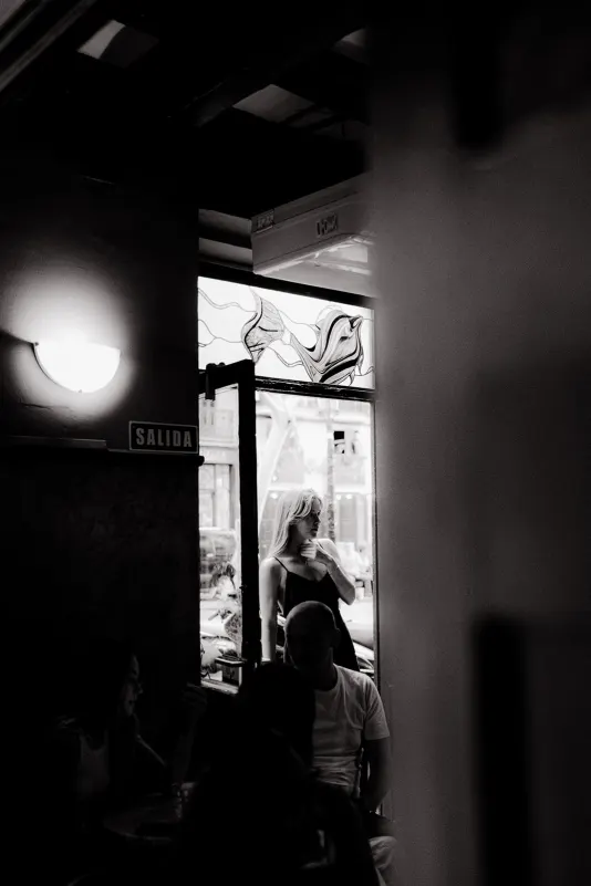 Woman in a black dress stands thoughtfully in a café doorway, captured during a Vacation Portraits photoshoot abroad.