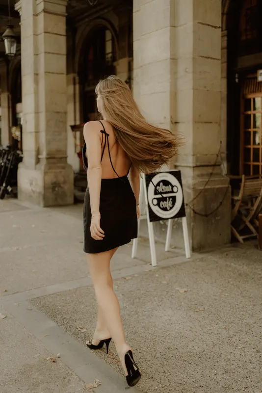 Woman in a black dress strolls past a café with flowing hair during a Vacation Portraits photoshoot in the city.
