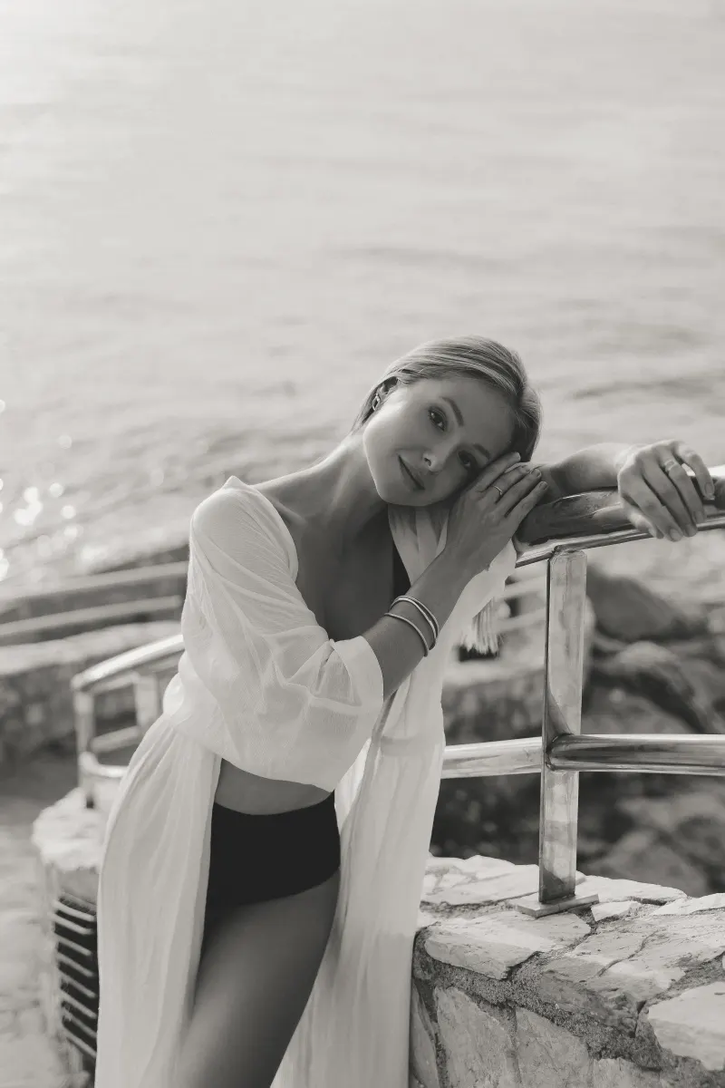 Woman in a swimsuit and sheer cover-up leans on a seaside railing, captured during a Vacation Portraits photoshoot.