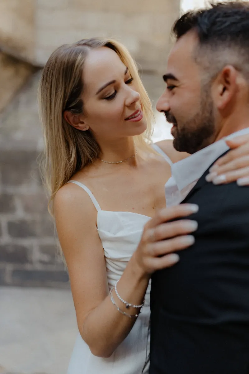 Woman in a white dress gazes lovingly at her partner during a couples & engagements photoshoot in a historic city setting.