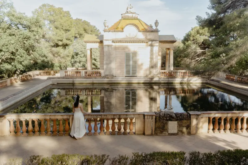 Woman in a white dress gazes over a tranquil pond at a classical pavilion, captured during a couples & engagements session.