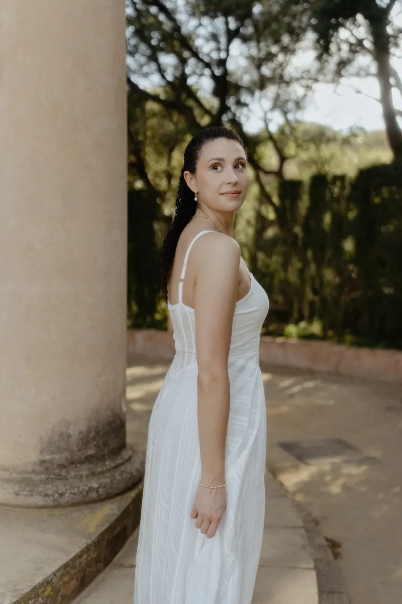 Woman in a white dress glances back with a soft smile, captured during a couples & engagements session at a garden pavilion.